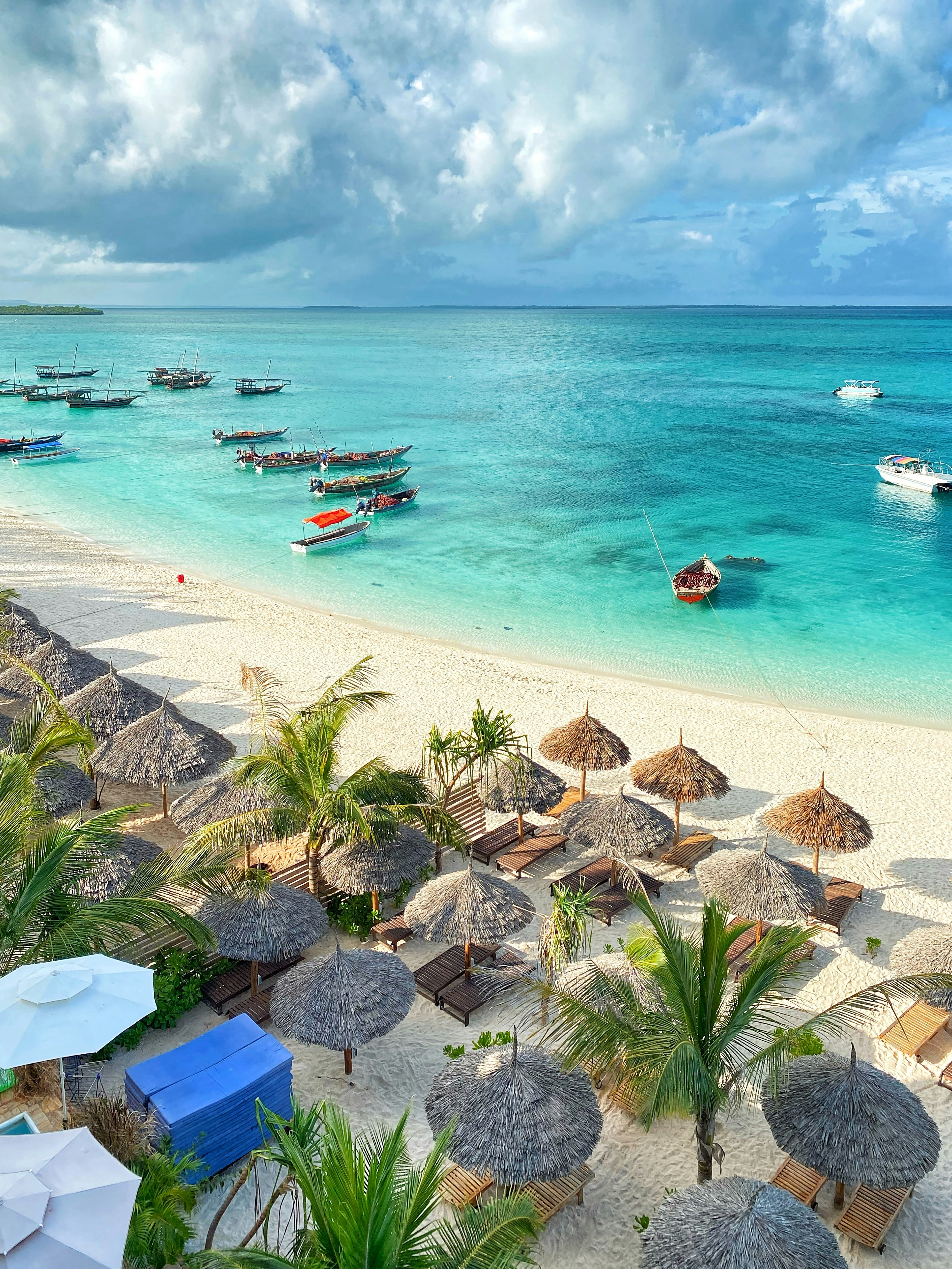 Zanzibar beach hotel area with thatched umbrellas, loungers, boats, and bright ocean water